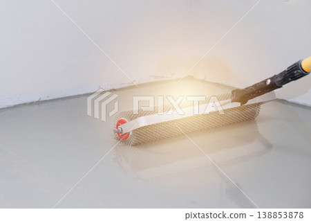 Roller for self-leveling floor. Worker applies coating with roller on concrete surface in indoor location during daylight hours Roller for self-leveling floor. Worker applies coating with roller on concrete surface in indoor location during daylight hours 138853878
