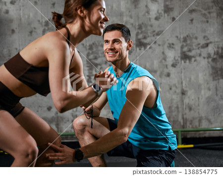 Woman performing squat while man assists with form during gym training session. Woman performing squat while man assists with form during gym training session. 138854775