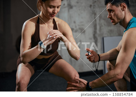 Woman performing squat exercise while man monitors technique in gym. Woman performing squat exercise while man monitors technique in gym. 138854784