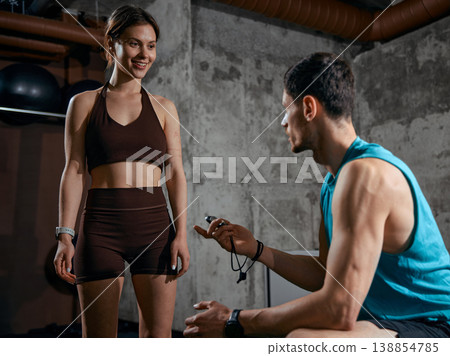 Man holding stopwatch giving instructions to woman during strength training session 138854785