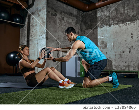 Personal trainer assisting woman with medicine ball during core workout session. Personal trainer assisting woman with medicine ball during core workout session. 138854860