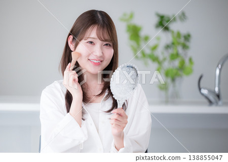 一張特寫鏡頭,一位女士對著手鏡塗抹腮紅,展現了她自然的妝容和美容護理習慣。 一張特寫鏡頭,一位女士對著手鏡塗抹腮紅,展現了她自然的妝容和美容護理習慣。 138855047