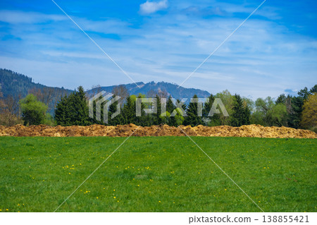 Green meadow with grass and organic manure fertilizer pile in field, soil enrichment, sustainable farming, rural landscape with forest and mountains Green meadow with grass and organic manure fertilizer pile in field, soil enrichment, sustainable farming, rural landscape with forest and mountains 138855421