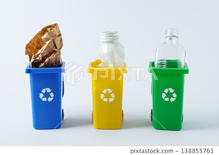 Sorting and recycling waste, three toy recycling bins for glass, paper, and plastic on white background. Color coded containers promoting eco friendly waste sorting and sustainable living. Sorting and recycling waste, three toy recycling bins for glass, paper, and plastic on white background. Color coded containers promoting eco friendly waste sorting and sustainable living. 138855761