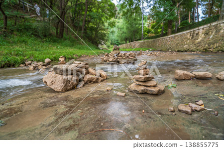A vertical stack of smooth river stones balanced on a rocky riverbed with mountains and cloudy sky in the background. Natural landscape, calm atmosphere, balance, and harmony in nature. A vertical stack of smooth river stones balanced on a rocky riverbed with mountains and cloudy sky in the background. Natural landscape, calm atmosphere, balance, and harmony in nature. 138855775