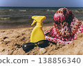 Sunscreen spray bottle with sunglasses and hat on sandy beach near sea Summer vacation concept with sun protection and copy space 138856340