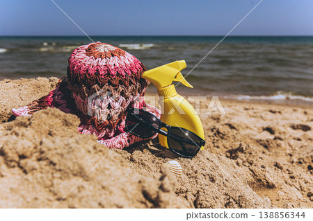 Sunscreen spray bottle with sunglasses and hat on sandy beach near sea Summer vacation concept with sun protection and copy space 138856344