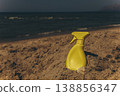 Sunscreen spray bottle placed on sandy shore with sea in background Beach skincare product concept under warm sunlight 138856347