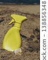 Sunscreen spray bottle placed on sandy shore with sea in background Beach skincare product concept under warm sunlight 138856348