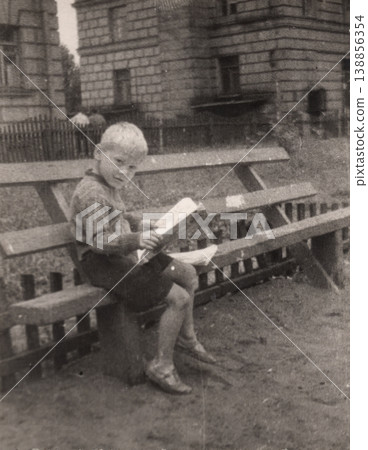 Vintage boy sitting on bench reading book outdoors 1950s 138856354