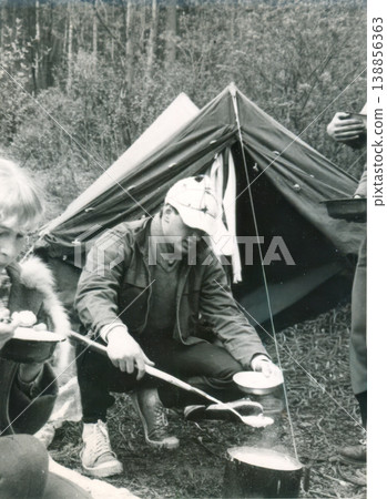 Young man cooking at campsite near tent in forest 1960s Young man cooking at campsite near tent in forest 1960s 138856363