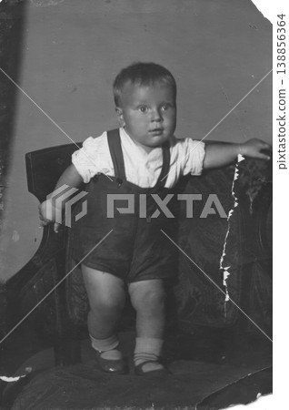 Vintage toddler boy in suspenders standing on armchair studio portrait Vintage toddler boy in suspenders standing on armchair studio portrait 138856364