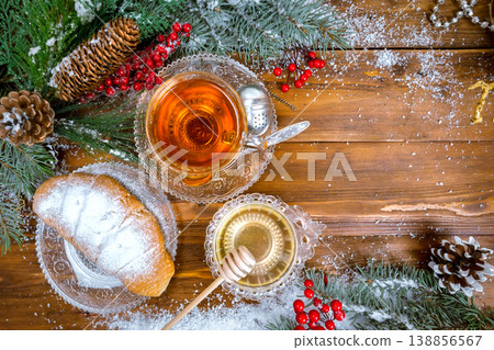 Christmas background, cup of tea with honey and croissant, branch of a Christmas tree in the snow.Top view Christmas background, cup of tea with honey and croissant, branch of a Christmas tree in the snow.Top view 138856567