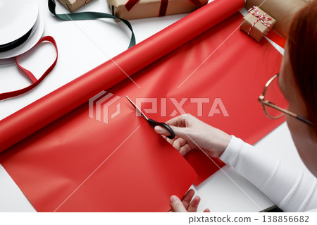 Woman cutting wrapping paper preparing gift packaging for festive celebration Woman cutting wrapping paper preparing gift packaging for festive celebration 138856682