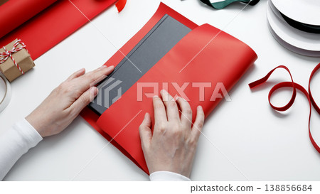 Woman wrapping book with red gift paper preparing thoughtful present Woman wrapping book with red gift paper preparing thoughtful present 138856684
