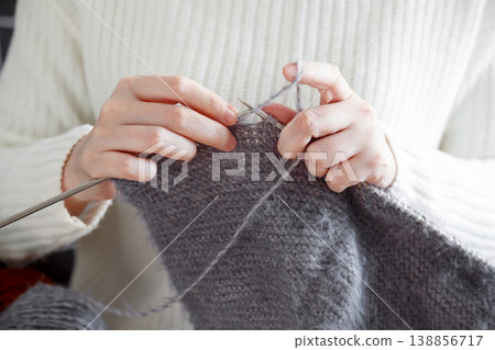Wearing a white sweater, woman crafts cozy handmade fabric using knitting needles 138856717