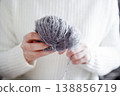 Woman in white sweater winding yarn ball by hand for knitting or craft project 138856719