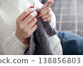 Woman wearing white sweater knitting with needles crafting cozy handmade fabric 138856803