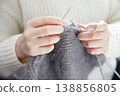 Hands of a woman in a white sweater crafting cozy fabric with knitting needles 138856805