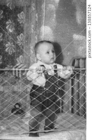 Vintage baby standing in mesh playpen holding rail 1950s Vintage baby standing in mesh playpen holding rail 1950s 138857124