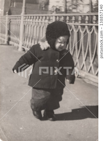 Vintage toddler walking outdoors in winter coat and fur hat Vintage toddler walking outdoors in winter coat and fur hat 138857140