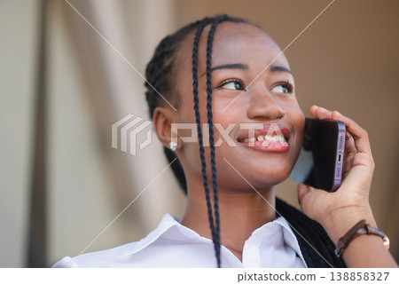 Close up of young Black business woman smiling during smartphone call outdoors, looking away with confidence. Mobile communication, customer service, remote work and modern lifestyle concept. Close up of young Black business woman smiling during smartphone call outdoors, looking away with confidence. Mobile communication, customer service, remote work and modern lifestyle concept. 138858327