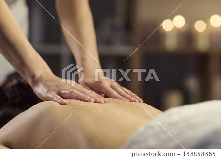 Therapist hands massaging back in spa with warm candles and calming ambiance Therapist hands massaging back in spa with warm candles and calming ambiance 138858365