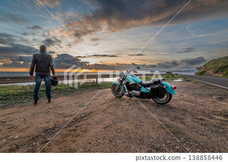 Biker standing by a classic motorcycle by the sea 138858446