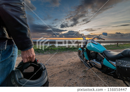 Biker with a helmet on his hand stands by a motorcycle 138858447