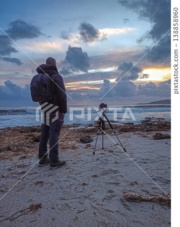 Male Photographer Standing by DSLR on Tripod on Beach at Sunset Male Photographer Standing by DSLR on Tripod on Beach at Sunset 138858960