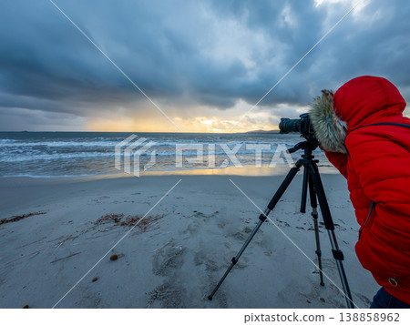 Female Photographer Looking Through DSLR Viewfinder on Tripod on Beach at Sunset Female Photographer Looking Through DSLR Viewfinder on Tripod on Beach at Sunset 138858962