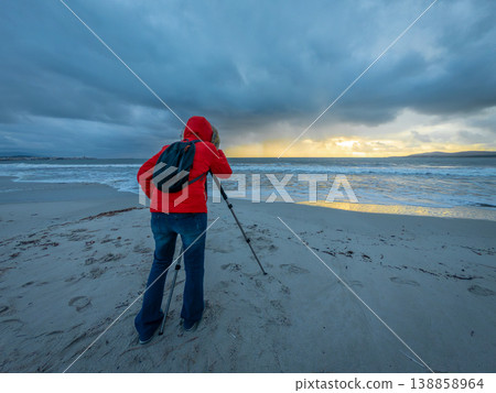 Female Photographer Shooting with DSLR on Tripod at Sunset on Beach during Stormy Waves Female Photographer Shooting with DSLR on Tripod at Sunset on Beach during Stormy Waves 138858964