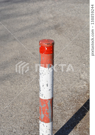 Red and white weathered traffic bollard on asphalt Red and white weathered traffic bollard on asphalt 138859244