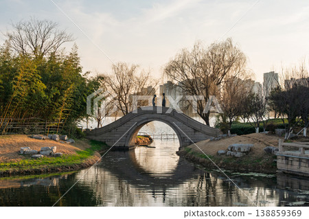 Stone arch bridge with two stylized figures arches over a peaceful canal. Stone arch bridge with two stylized figures arches over a peaceful canal. 138859369