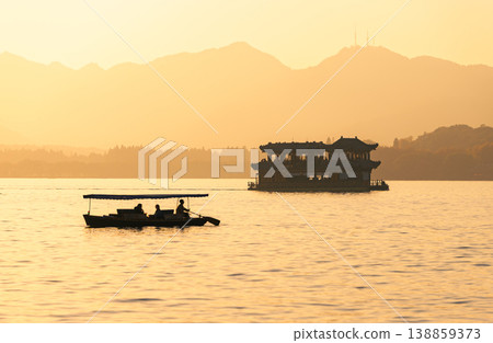 Golden sunset over West Lake with traditional boats carrying passengers in Hangzhou, China Golden sunset over West Lake with traditional boats carrying passengers in Hangzhou, China 138859373