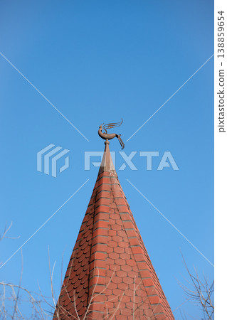 Metal weather vane in the shape of a bird . The image conveys a sense of symbolism, craftsmanship, and classic European rooftop design. Metal weather vane in the shape of a bird . The image conveys a sense of symbolism, craftsmanship, and classic European rooftop design. 138859654