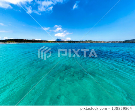 Low angle view of turquoise water at Lu Impostu beach with Tavolara island and cloudy blue sky Low angle view of turquoise water at Lu Impostu beach with Tavolara island and cloudy blue sky 138859864