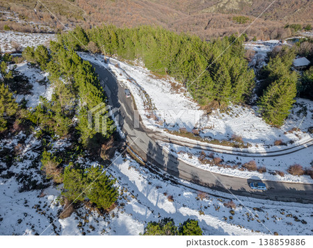 Mountain Road surrounded by snow Viewed from Above with Green Pine Trees and Two Cars 138859886