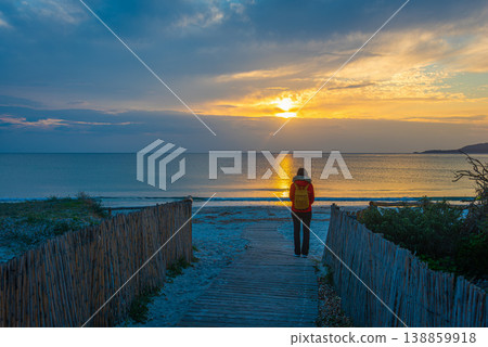 Woman Standing on Beach Path at Sunset with Calm Sea and Clouds Woman Standing on Beach Path at Sunset with Calm Sea and Clouds 138859918