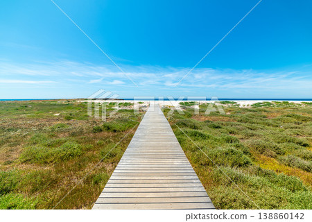 Wooden Boardwalk Leading to White Sand Beach under Blue Sky in Spring, Sardinia Wooden Boardwalk Leading to White Sand Beach under Blue Sky in Spring, Sardinia 138860142