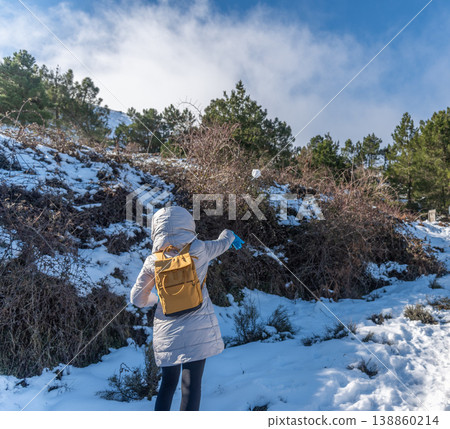 Woman in Winter Clothes Throwing a Snowball in Snowy Landscape Seen from Behind 138860214