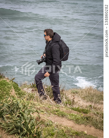 Vertical View of Photographer Walking on Coast with Backpack and Camera Vertical View of Photographer Walking on Coast with Backpack and Camera 138860282