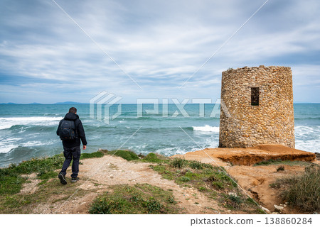 Hiker with Backpack Walking Towards Observation Tower by the Sea under Gray Sky Hiker with Backpack Walking Towards Observation Tower by the Sea under Gray Sky 138860284
