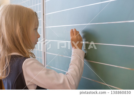 First grade pupil a girl writing on green blackboard at school lesson First grade pupil a girl writing on green blackboard at school lesson 138860830