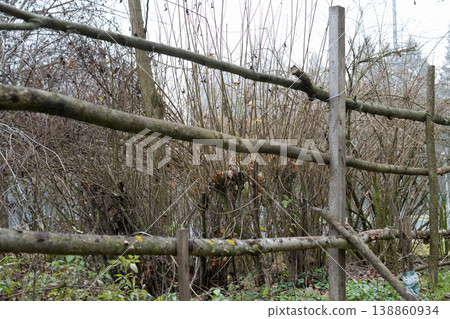 Eco-friendly garden fencing. Handmade wooden barrier in a park or backyard. Old rustic fence against a background of bare bushes and trees in early spring. Eco-friendly garden fencing. Handmade wooden barrier in a park or backyard. Old rustic fence against a background of bare bushes and trees in early spring. 138860934