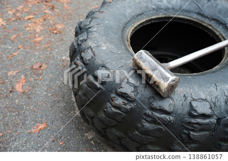 Wheel and metal sledgehammer for outdoors training . Developing strength, speed and endurance for an athlete 138861057