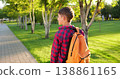 Happy child boy outdoors walks along park path at sunset. Schoolboy boy with backpack smiles. Happy child goes to school. Joyful kid outdoors enjoying nature, golden sunlight, and peaceful walk. 138861165