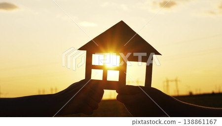 Silhouette of hands holding paper house at sunset. Sun rays shine through window, highlighting financial planning, home investment, and future opportunities for wealth and stability. 138861167