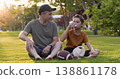 Happy father son relax on grass in park after playing ball. Joyful boy drinks water shares dad. Smiling father son enjoy sunset bonding outdoors. Family sport hydration healthy lifestyle golden hour. 138861178