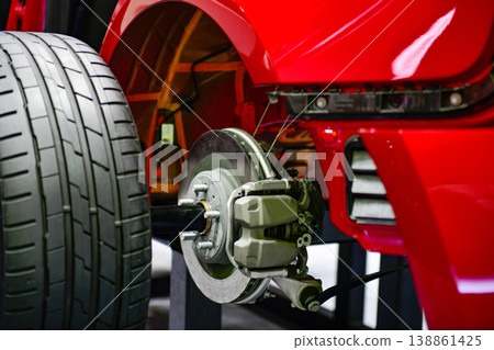 Close-up of a modern vehicle's rear suspension system, featuring disc brakes, calipers, and alloy wheels on a red car chassis display Close-up of a modern vehicle's rear suspension system, featuring disc brakes, calipers, and alloy wheels on a red car chassis display 138861425